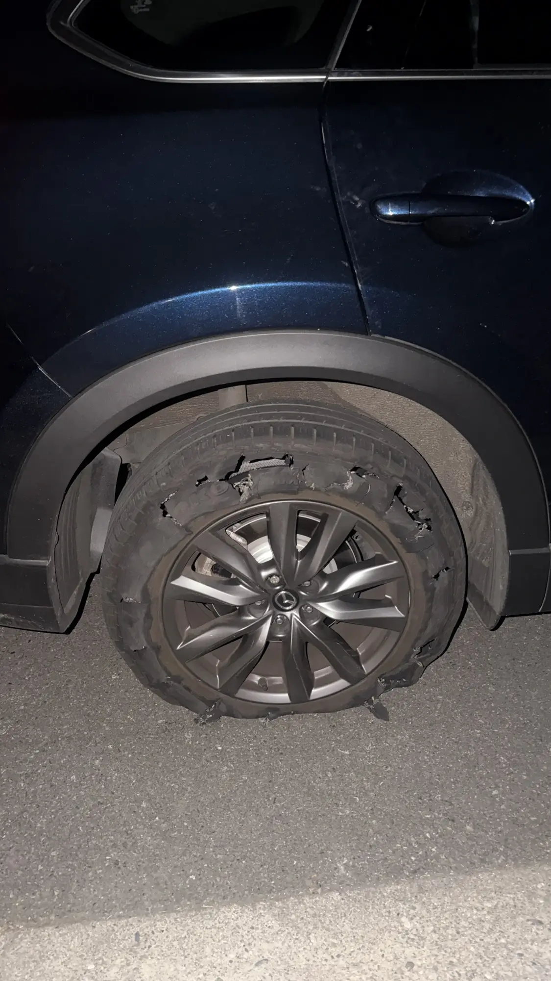 Severely shredded rear tire on a Mazda SUV needing roadside assistance